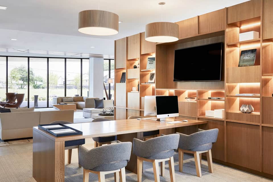 Modern office lounge with wooden wall shelving, pendant lights, and casual seating areas overlooking outdoor spaces