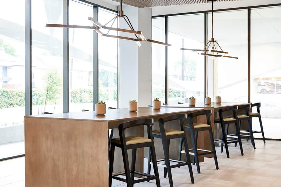 Modern office break room with long wooden counter, bar seating, and large windows
