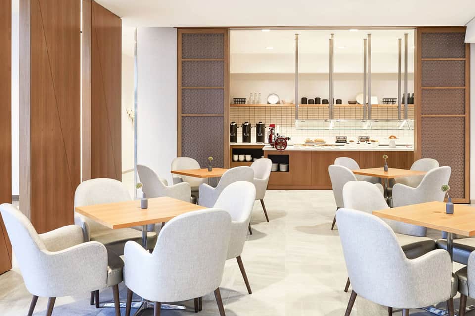 Modern café interior with wooden tables, cream chairs, shelving display, and contemporary design