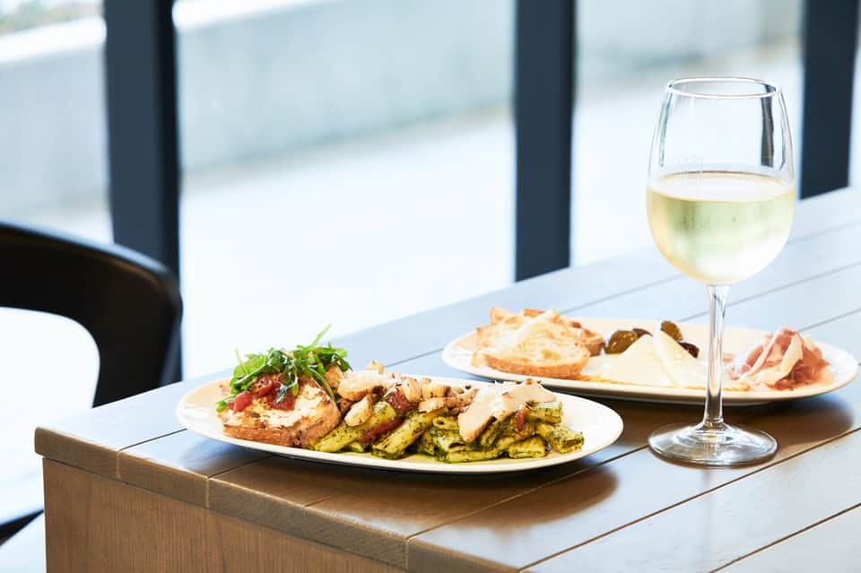 Elegant outdoor dining with white wine, grilled vegetables, and waterfront views through modern black-framed windows