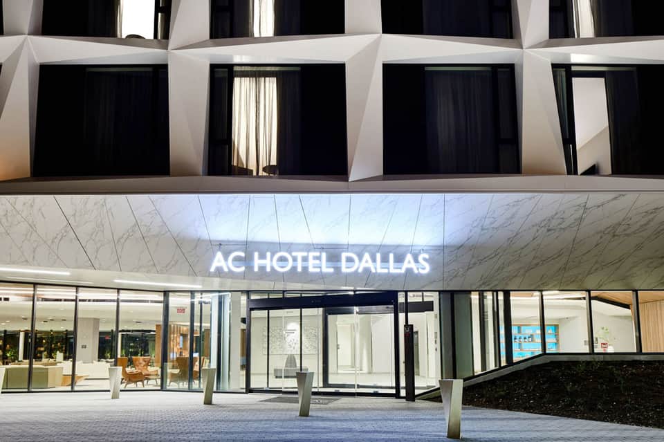 Modern AC Hotel Dallas entrance with illuminated signage and minimalist white facade at dusk