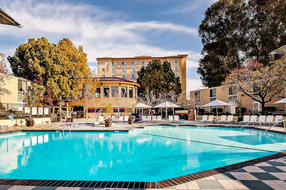 Resort pool with turquoise water, loungers, white umbrellas, and multi-story hotel building