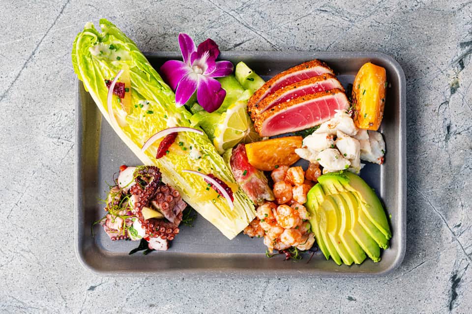 Elegant seafood platter with seared tuna, octopus, shrimp, avocado, and romaine lettuce on gray serving tray