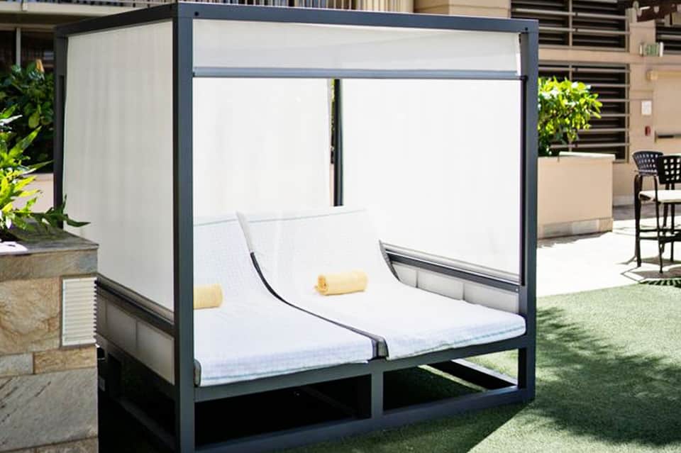 Modern outdoor daybed pavilion with white curtains and gray frame on manicured lawn