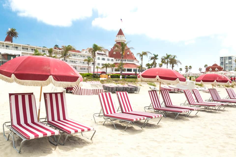 Beach scene with red and white striped lounge chairs, matching umbrellas, and Victorian-style hotel building in background