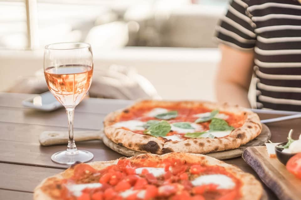 Rose wine glass and Margherita pizzas on outdoor dining table with striped shirt visible