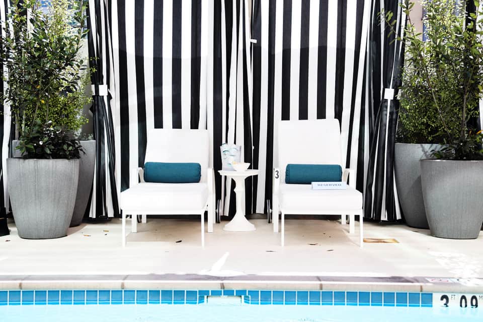 Two white lounge chairs under striped black and white canopy by poolside