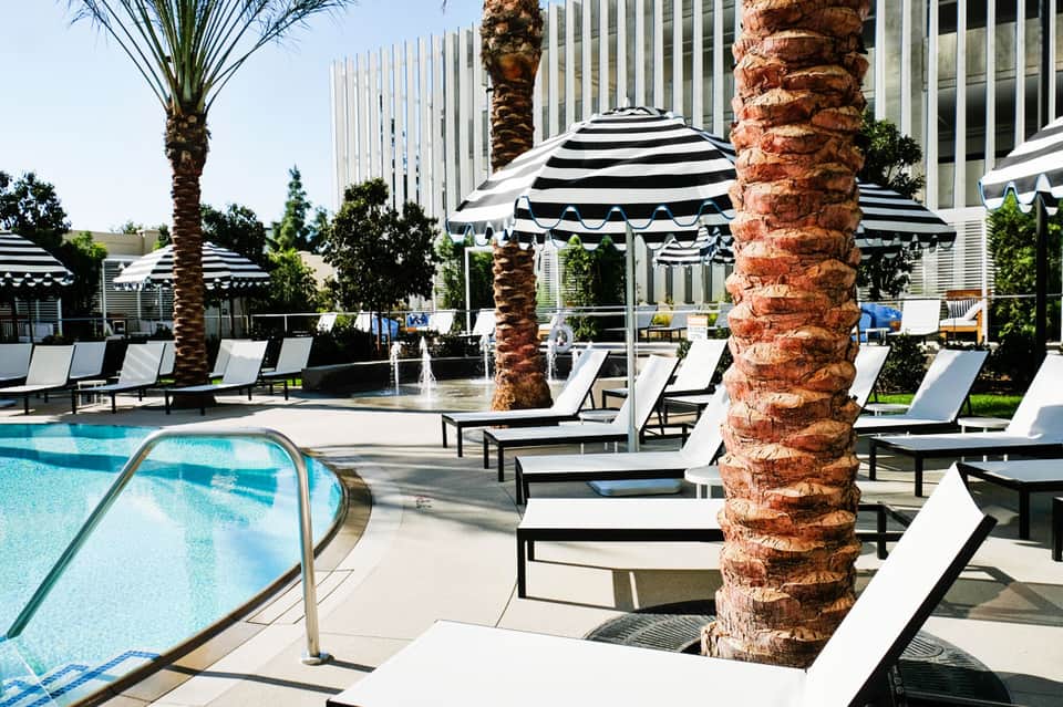 Luxury resort pool deck with striped umbrellas, lounge chairs, palm trees, and high-rise buildings