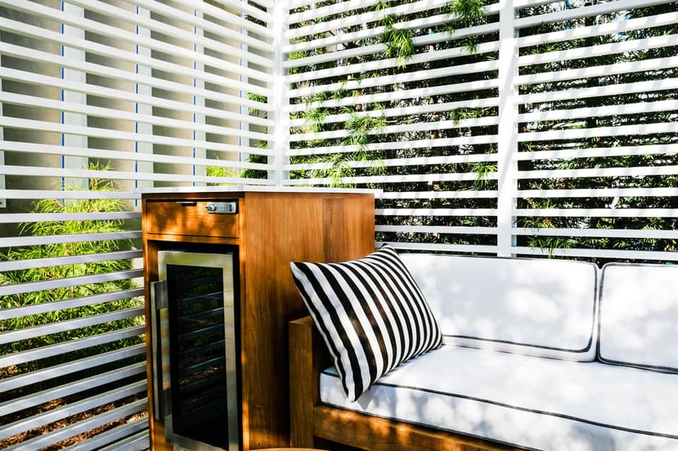 Modern patio with white sofa, striped pillow, and wood mini-fridge enclosed by horizontal privacy slats