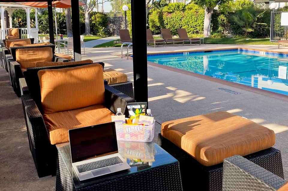 Covered lounge area with orange cushioned seating and glass table beside illuminated swimming pool