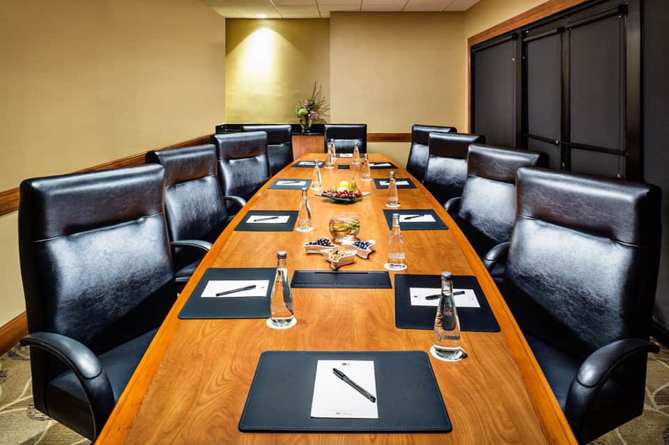 Executive boardroom with long wooden table, black leather chairs, and professional place settings