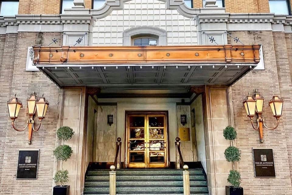 Historic brick hotel entrance with ornate orange awning, brass lanterns, and wooden doors flanked by topiary
