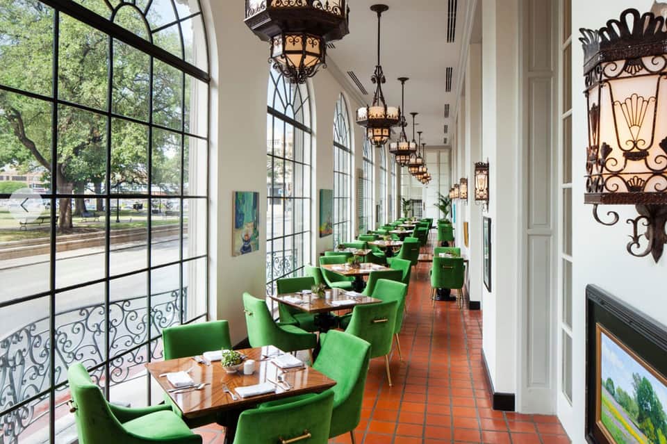 Elegant dining room with green velvet chairs, wooden tables, ornate chandeliers, and large windows overlooking gardens