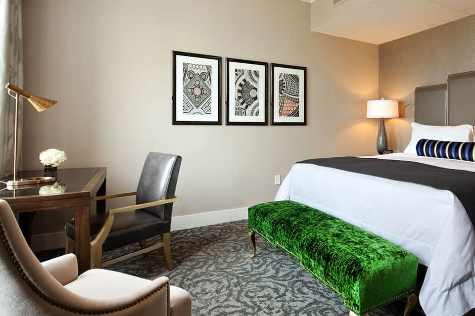 Contemporary hotel bedroom with king bed, desk, and framed artwork on neutral walls