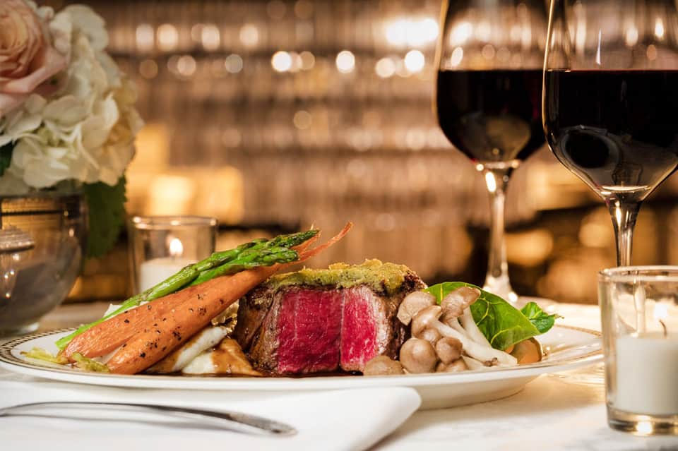 Fine dining plate with rare steak, roasted carrots, mushrooms, and asparagus paired with red wine