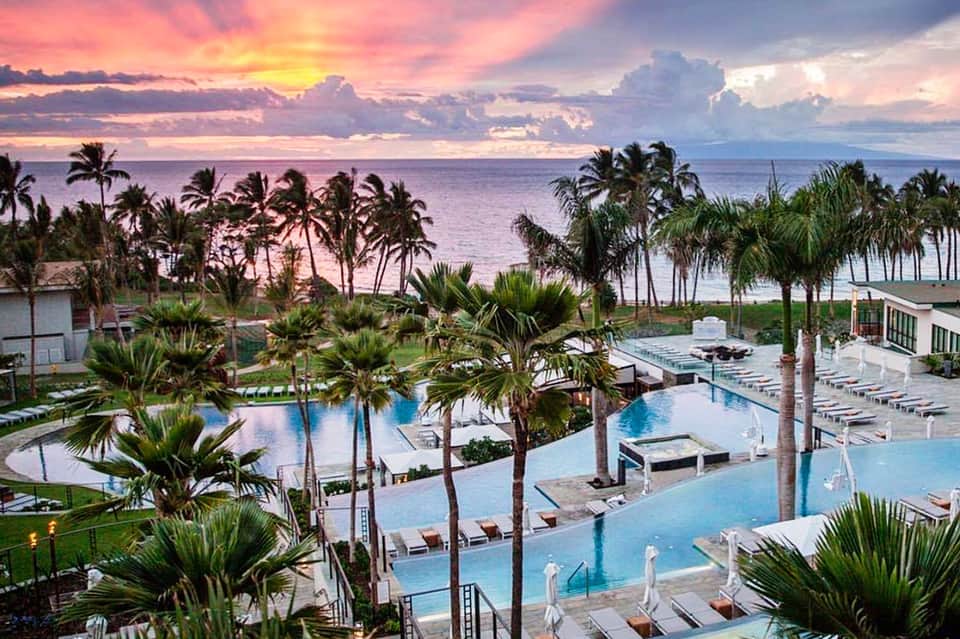 Luxury resort pool complex with palm trees at sunset, overlooking the ocean horizon