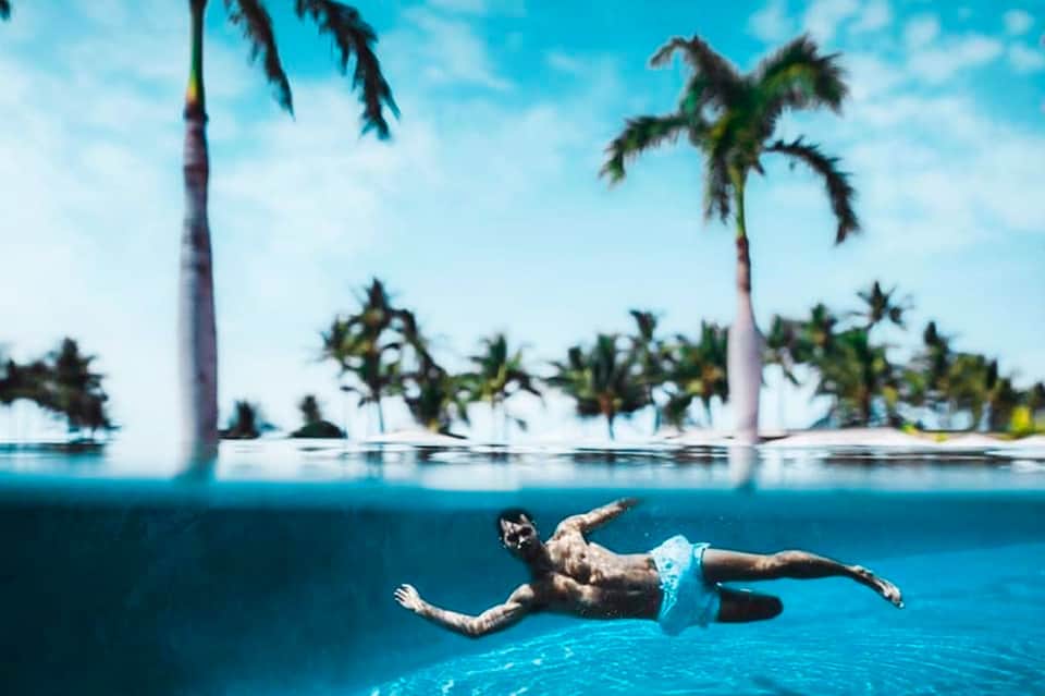 Man snorkeling underwater in tropical lagoon with palm trees and clear blue water