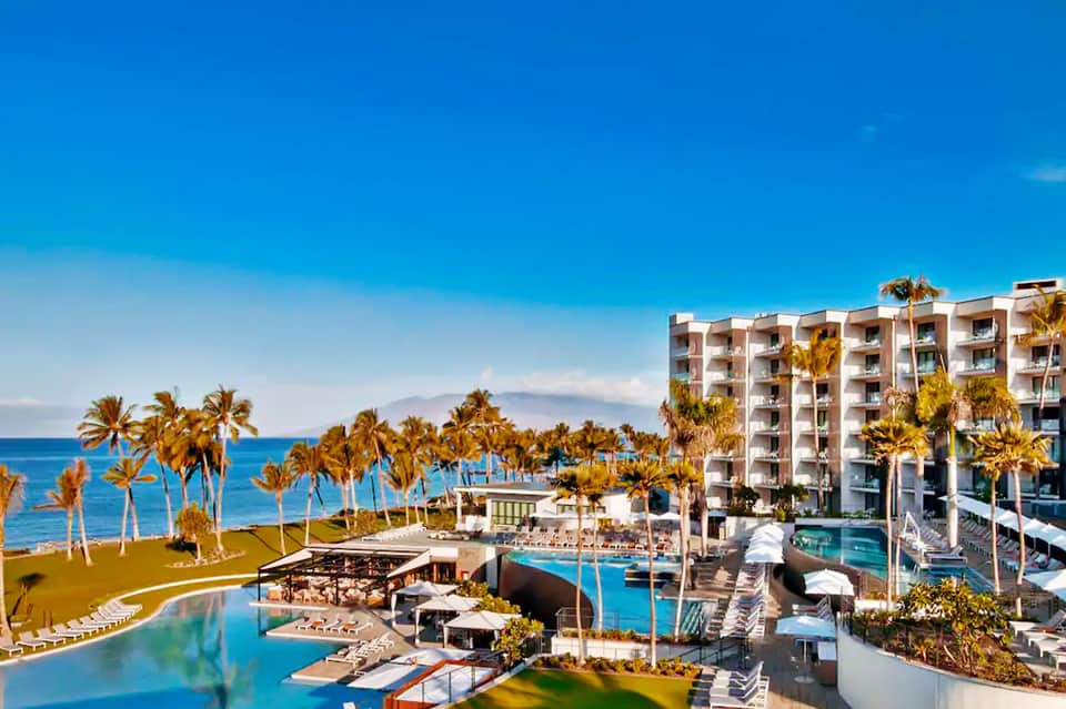 Beachfront resort with infinity pool, ocean views, palm trees, and modern architecture