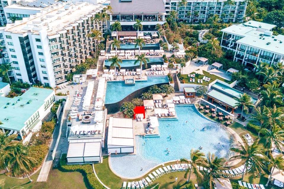 Aerial view of large resort complex with multiple pools, palm trees, and surrounding residential buildings