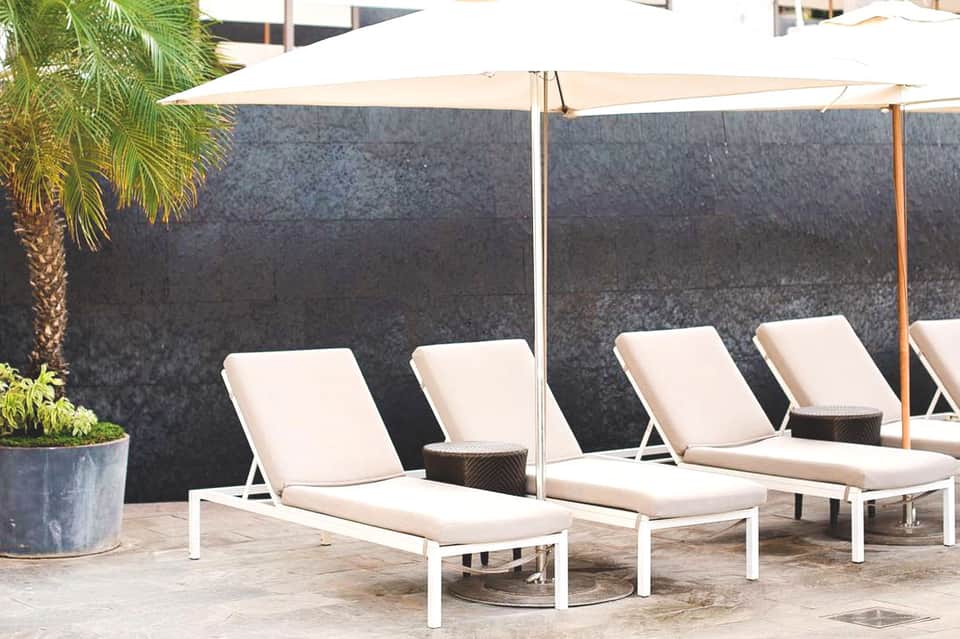Outdoor lounge area with white cushioned sun loungers under cream umbrellas against dark wall