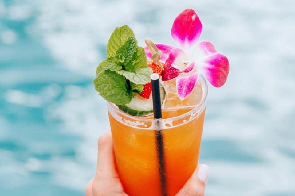 Colorful tropical cocktail garnished with pink orchid flower and mint leaves by the ocean
