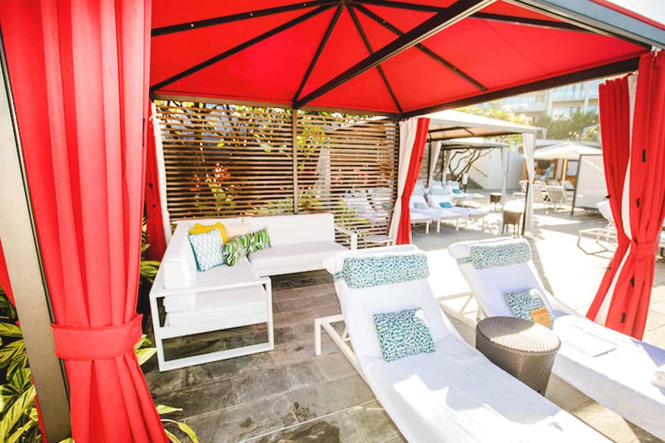 Red cabana with white loungers, patterned cushions, and wooden privacy screens
