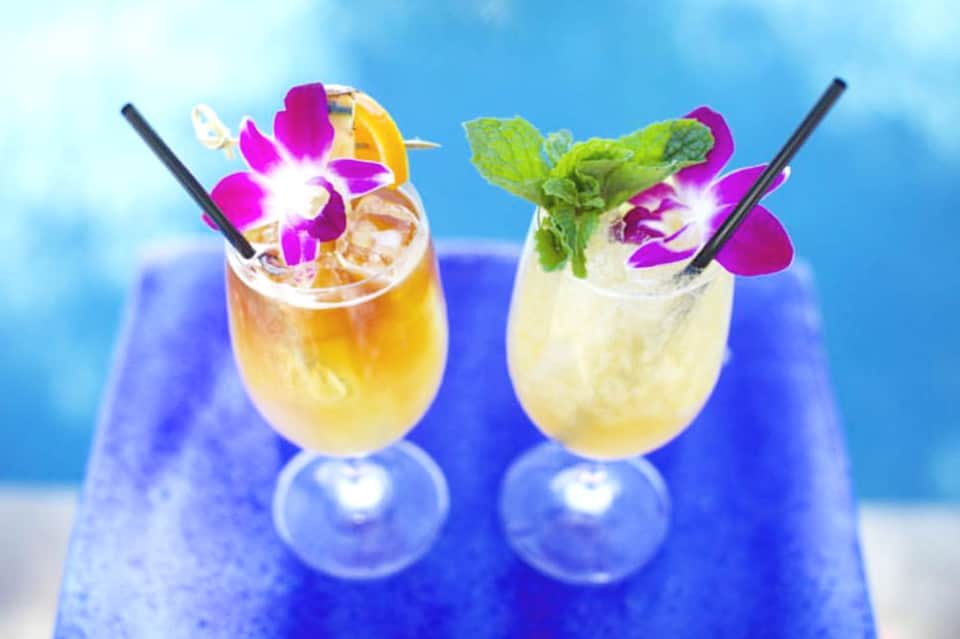 Two tropical cocktails garnished with orchid flowers and served with straws