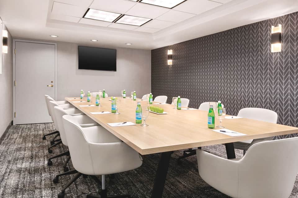 Modern conference room with long wooden table, white chairs, and patterned accent wall
