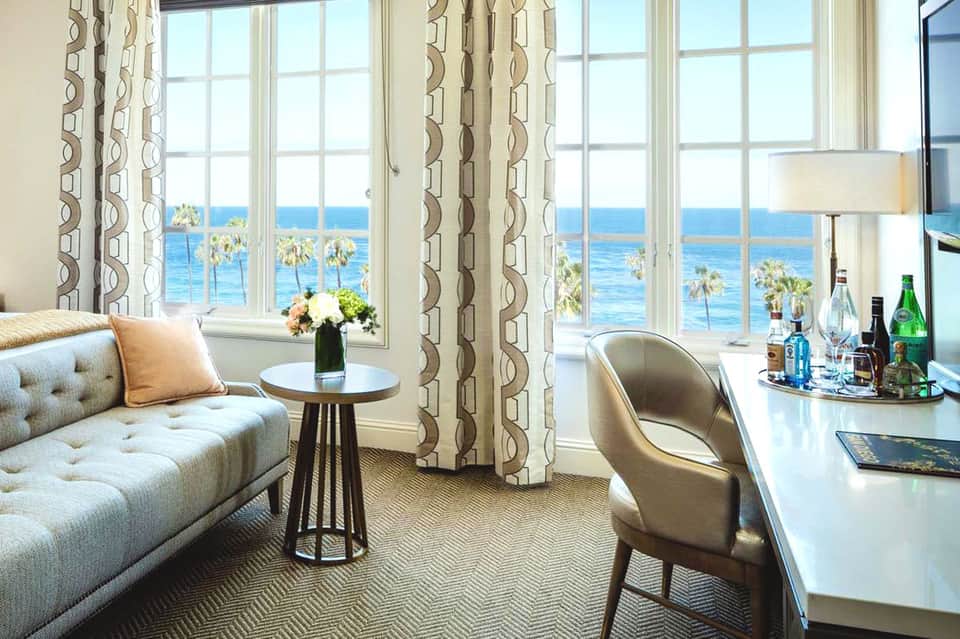 Luxury hotel suite with ocean view through large windows, modern furniture, and geometric patterned curtains