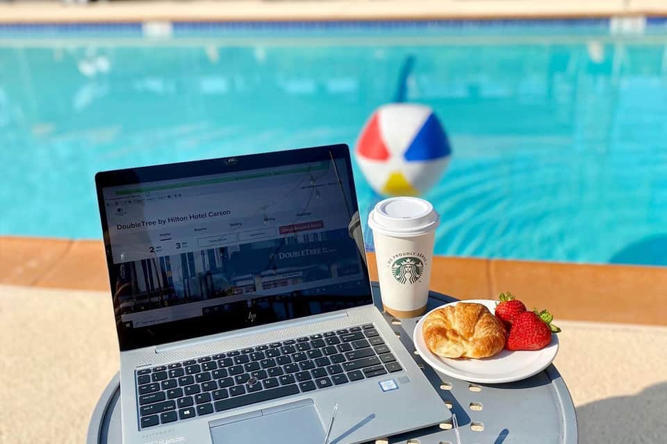 Laptop by a pool showing a hotel website, with Starbucks coffee and croissant on the table