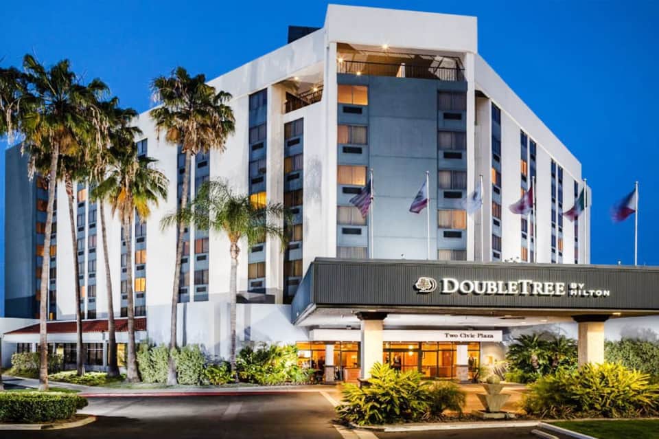 DoubleTree Hilton hotel exterior at dusk with white façade, palm trees, and illuminated entrance