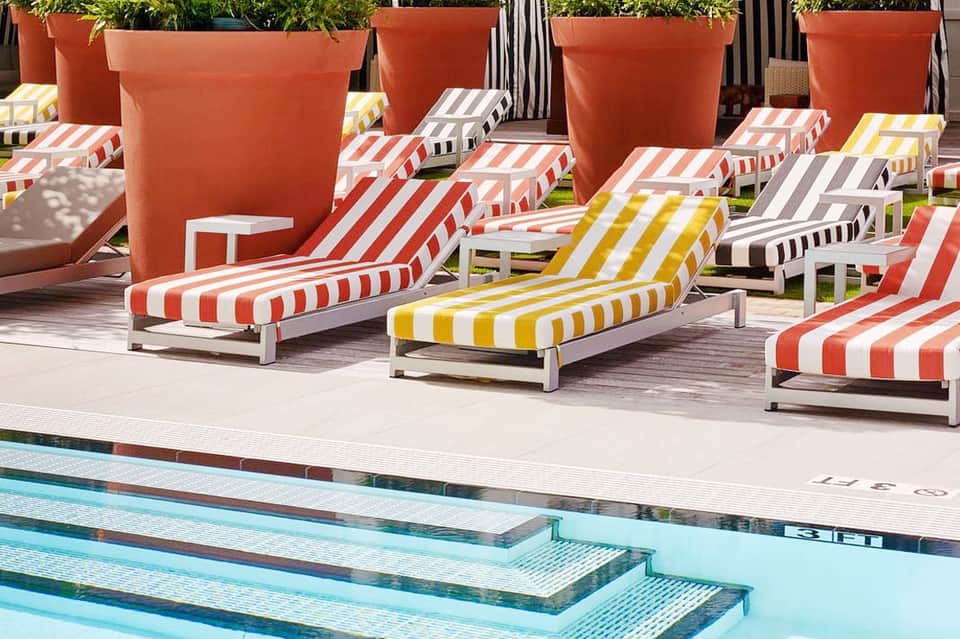 Colorful striped lounge chairs arranged around an outdoor swimming pool with large terracotta planters