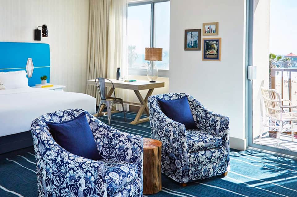 Modern hotel room with blue accent headboard, patterned chairs, and ocean view from private balcony