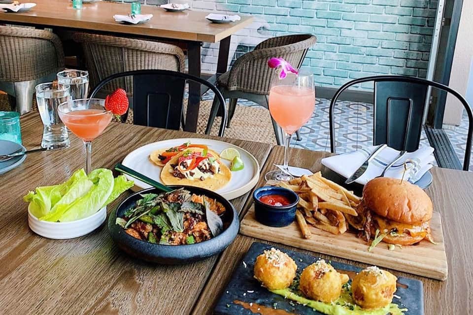 Outdoor restaurant patio with colorful cocktails, appetizers, burgers, and salads on wooden table