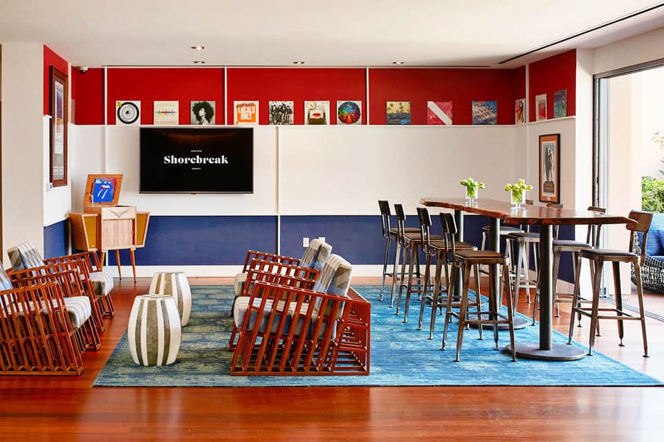 Modern hotel lounge with red accent wall, display shelves, bar seating, and contemporary furnishings