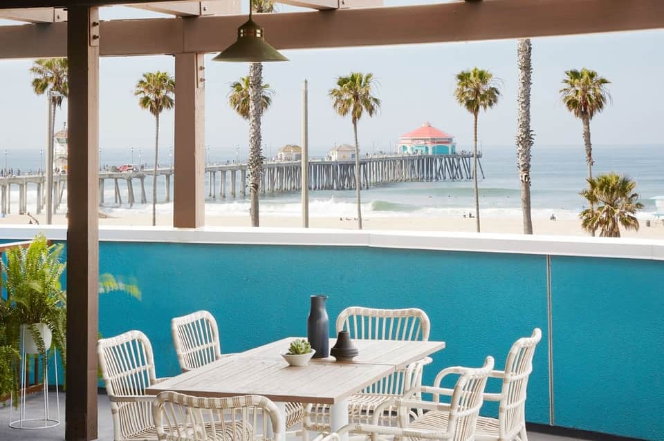 Beachfront dining area with white chairs, turquoise pool wall, and ocean pier views