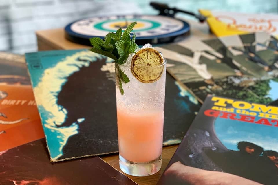 Tropical cocktail with lime slice and mint garnish on colorful magazines beside a dartboard