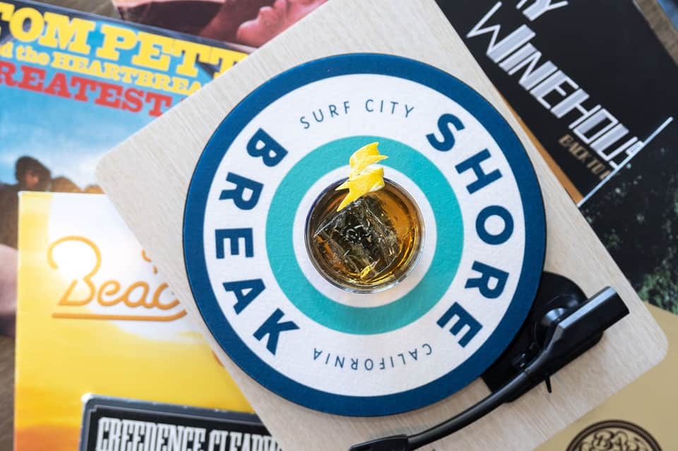 Surf City Brew Shop logo with golden beer bottle cap on colorful beach magazines