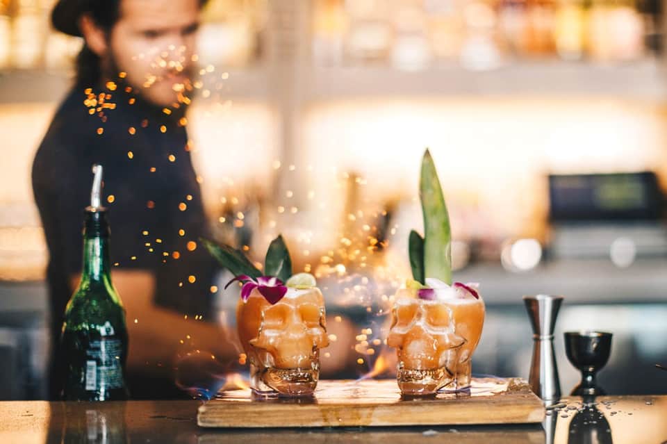Bartender pouring champagne into skull-shaped cocktail glasses with tropical garnish