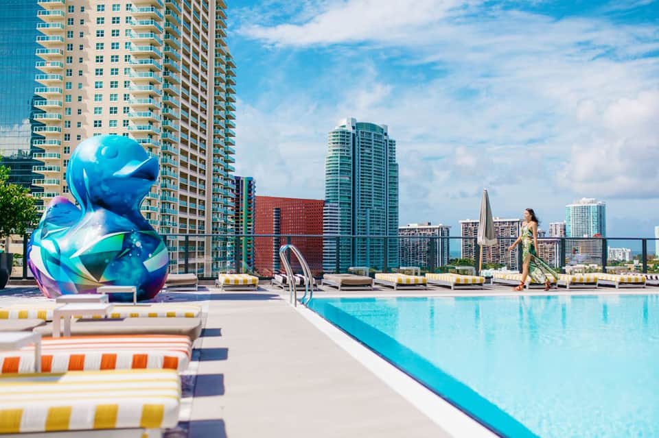 Rooftop pool deck with colorful loungers, blue water, and high-rise city skyline backdrop