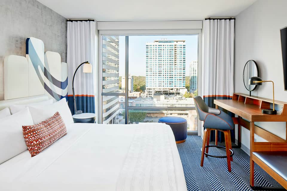 Modern hotel bedroom with city skyline views, white bedding, and contemporary furnishings