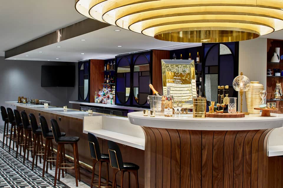Upscale bar interior with curved white counter, wooden accents, gold lighting, and premium liquor displays
