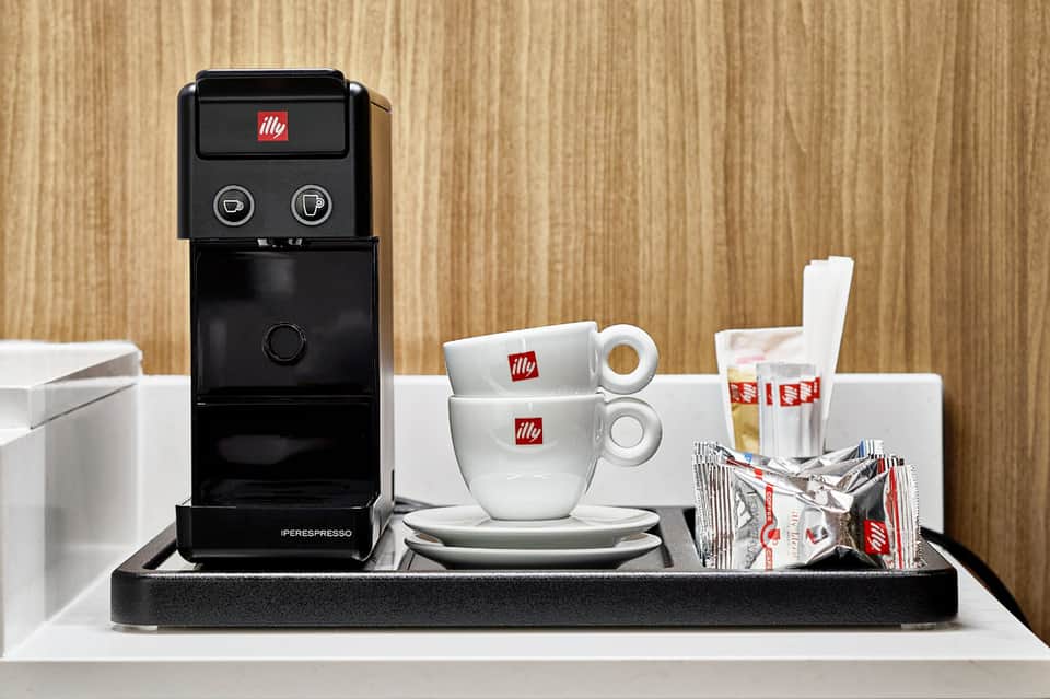 Black illy espresso machine with white branded cups and coffee packets on wooden counter