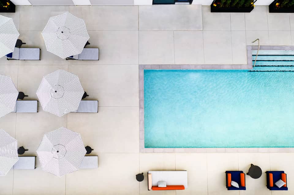 Aerial view of modern pool with white umbrellas, lounge chairs, and spa area