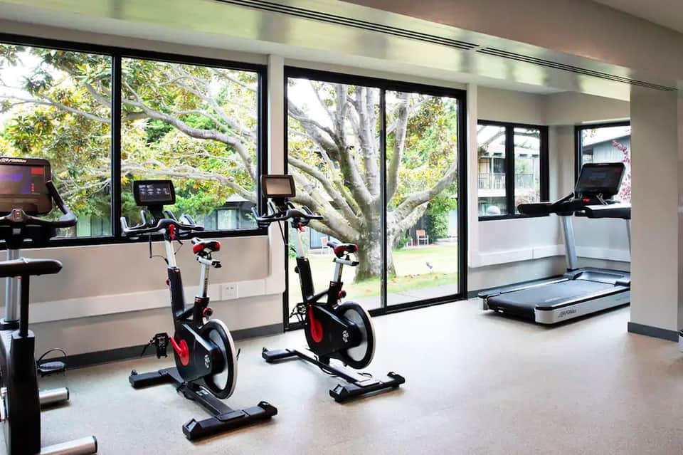 Modern fitness center with stationary bikes, treadmill, and large windows overlooking trees and grounds