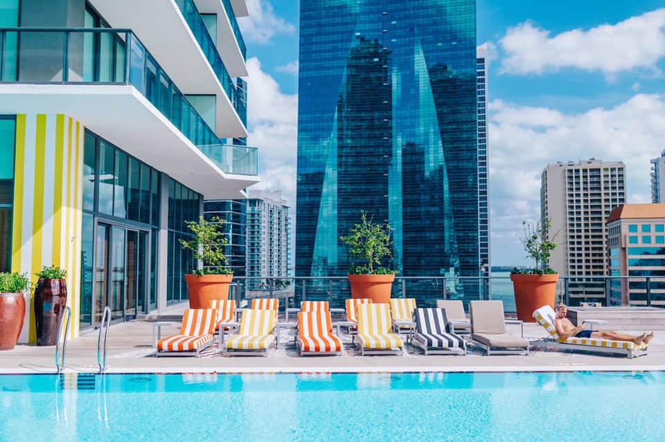 Modern rooftop pool with striped loungers overlooking city skyline and tall buildings