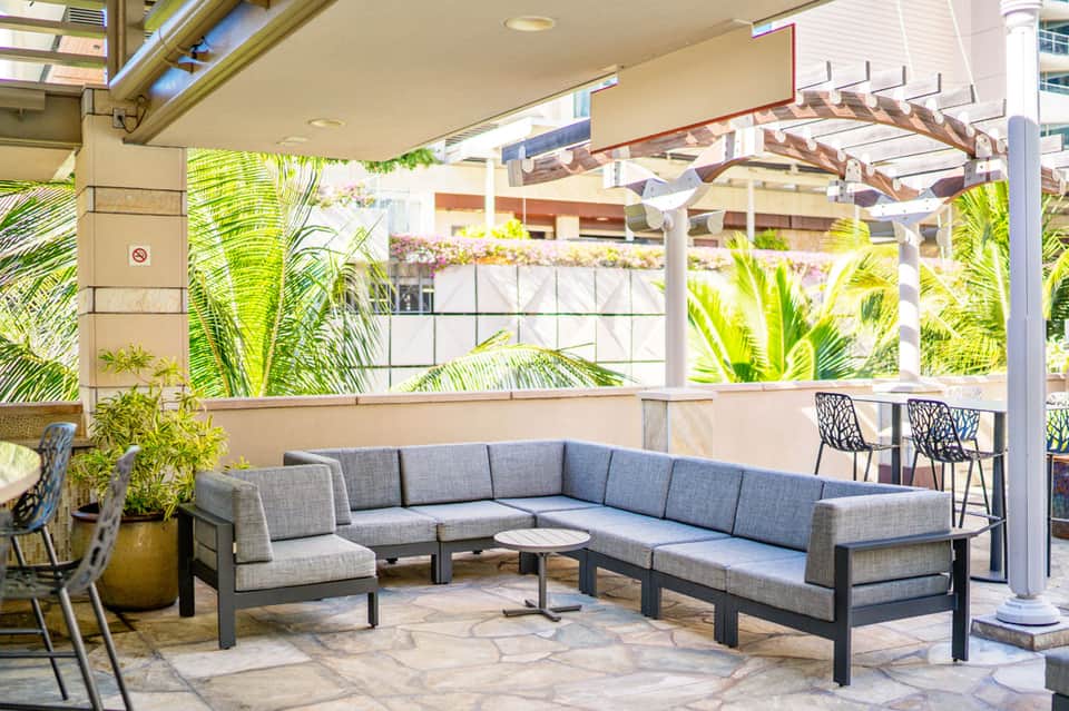 Covered patio seating area with gray sectional sofa and tropical plants