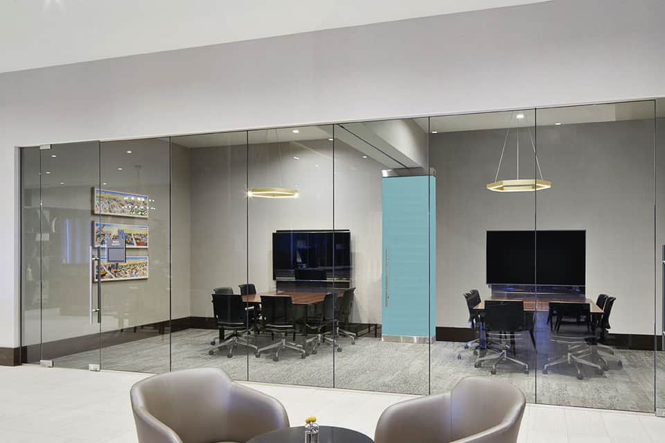 Modern office conference rooms with glass walls, black furniture, hanging lights, and gray carpeting