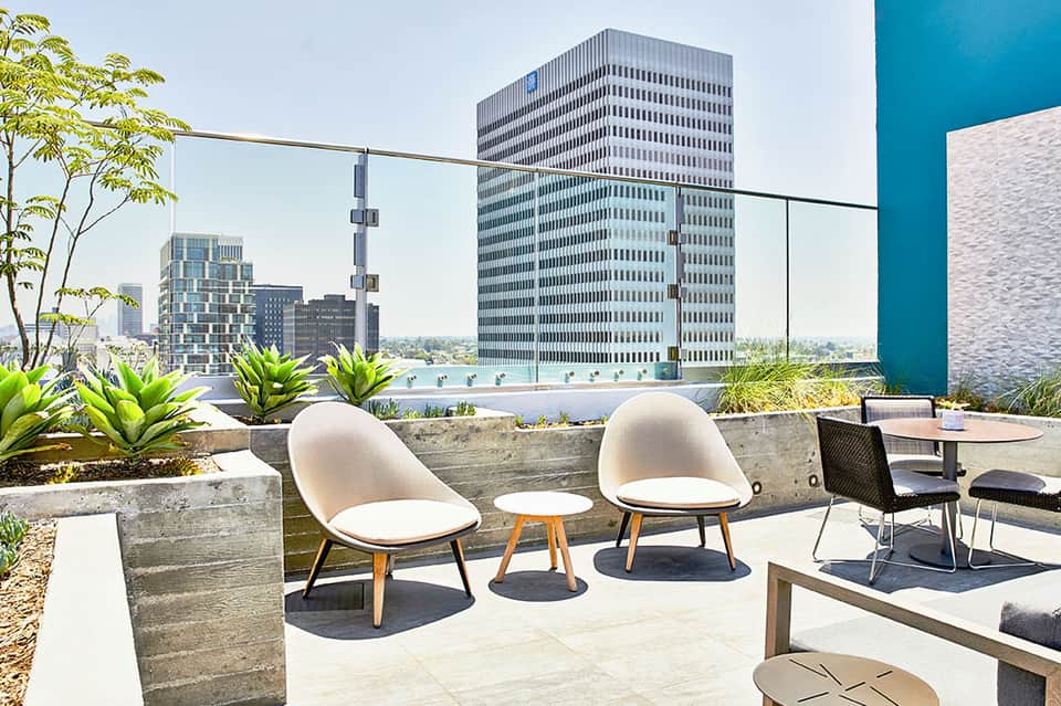 Rooftop lounge with modern chairs, planters, and city skyline views with pool in background