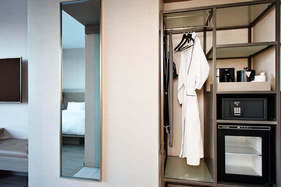 Modern hotel room closet with white robe hanging on dark shelving and microwave